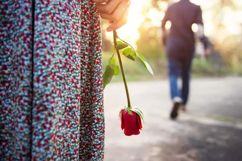 Closeup of a woman holding a rose as man walks away