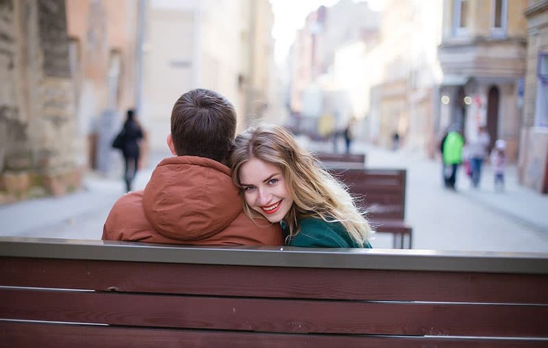 coppia sulla panchina con la donna sorridente rivolta verso l'uomo e appoggiata alla sua spalla