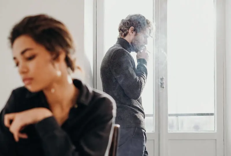 couple having a misunderstanding far from each other guy on the window smoking