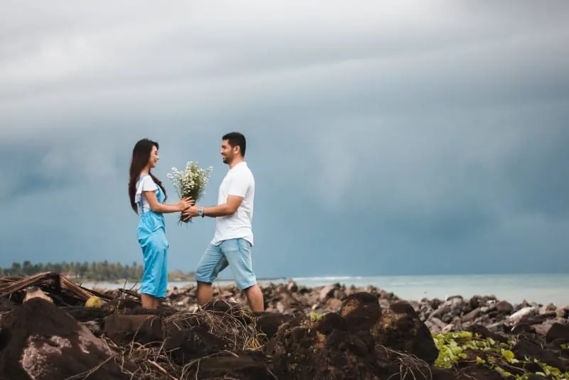 man in white shirt giving flowers to woman