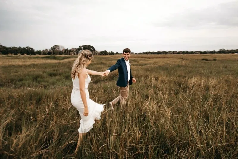 woman in white dress and man walking through grass