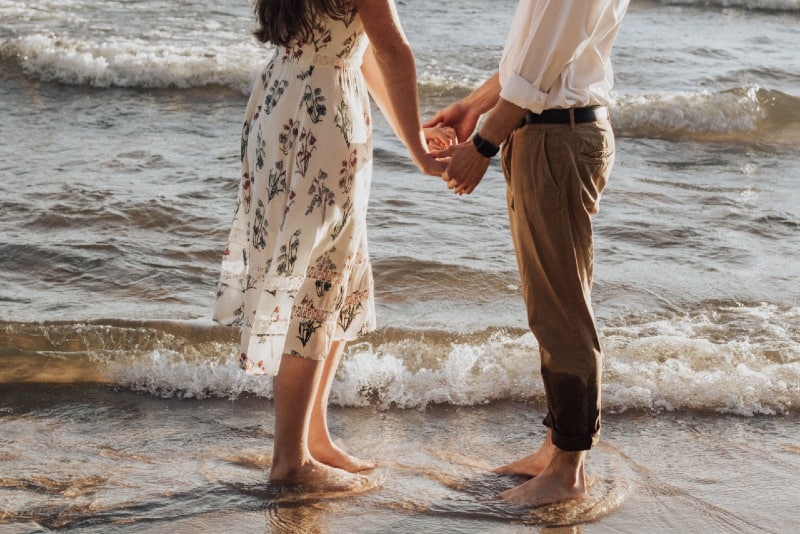 man and woman in floral dress holding hands on seashore