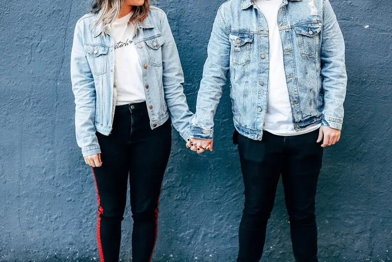woman and man in denim jackets holding hands beside wall