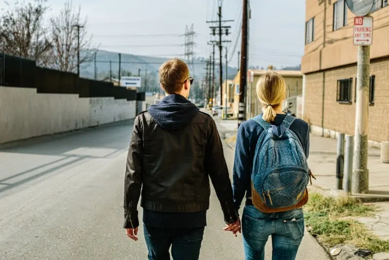 man and woman holding hands and walking on concrete road