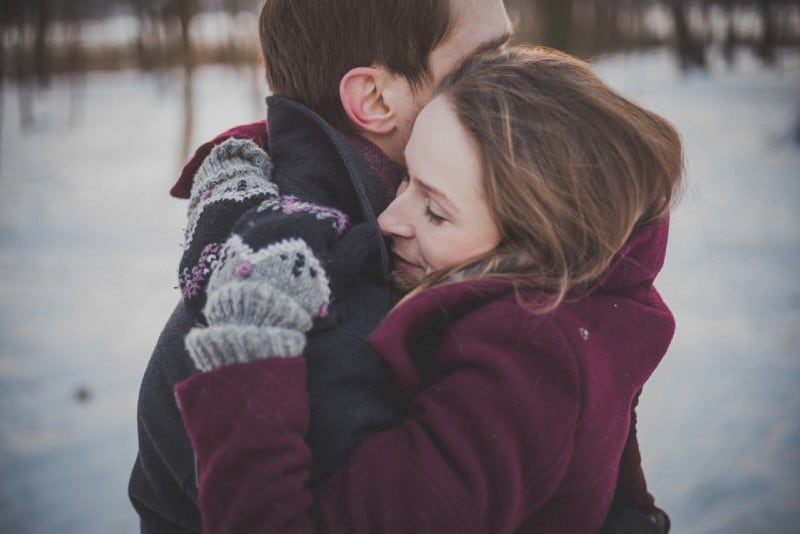 man in coat and woman in coat hugging in winter
