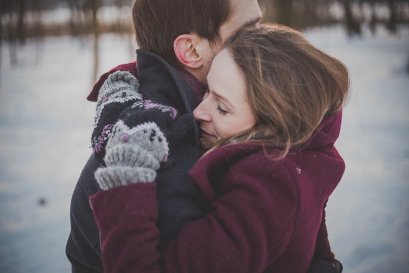 man and woman in coats hugging outdoor in winter