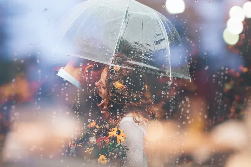 man and woman with flowers hugging under clear umbrella