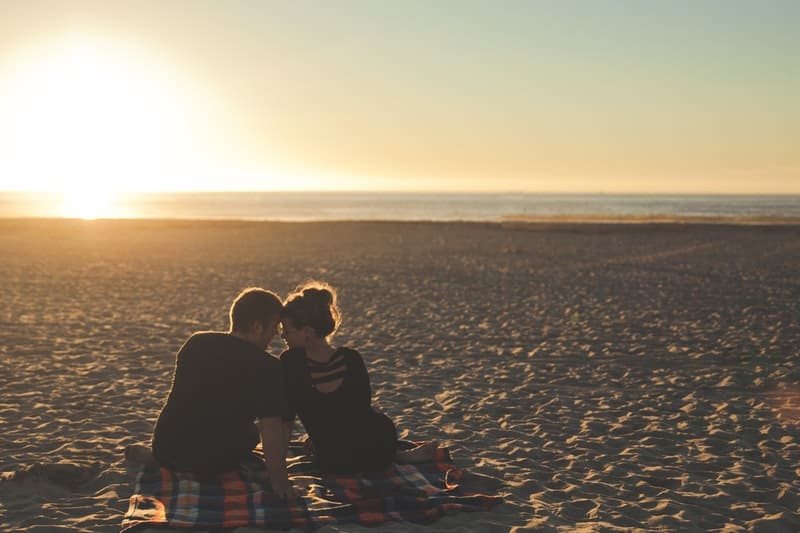 pareja en una esterilla de picnic frente a frente con la puesta/salida del sol frente a ellos