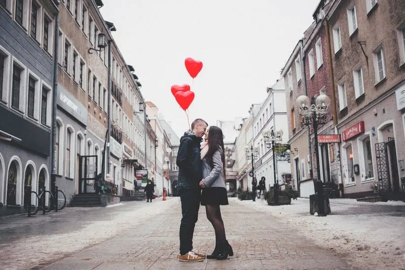 couple in the middle of the street kissing and carrying red heart balloons