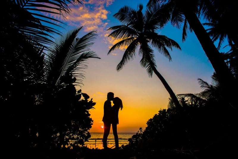 man and woman kissing near sea at sunset