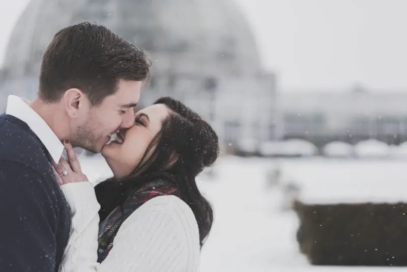 man and woman kissing and smiling on snow