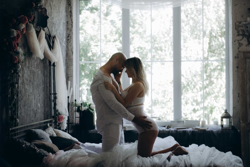 man and woman kneeling on bed beside window