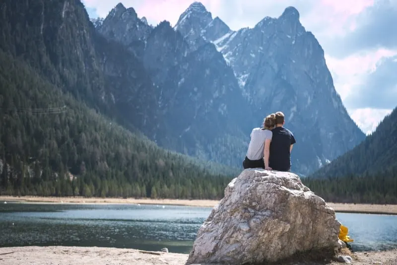 man and woman looking at mountain while sitting on rock