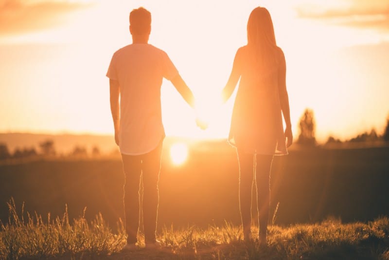 man and woman holding hands while facing sunset