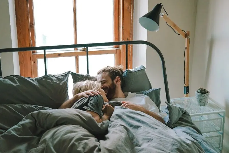 man kissing woman's forehead while lying in bed