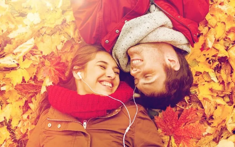 Couple with headhones lying on autumn leaves 