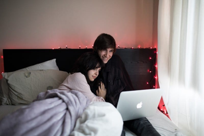 woman and man lying on bed and looking at laptop
