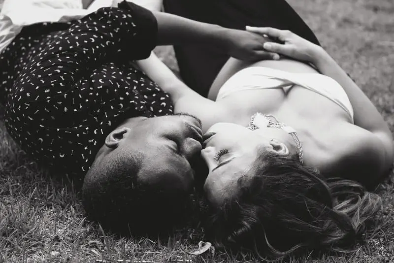 man and woman facing each other and lying on grass