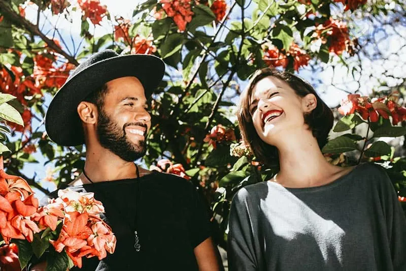 Couple by the flowering tree man wearing hat with grinning woman