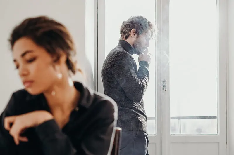 Couple misunderstanding woman sitting down man smoking