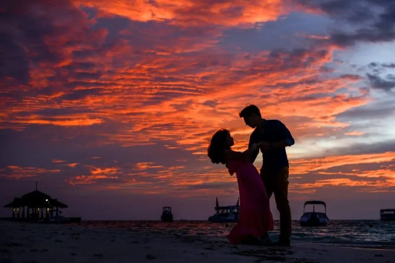 man and woman holding hands on beach during sunset