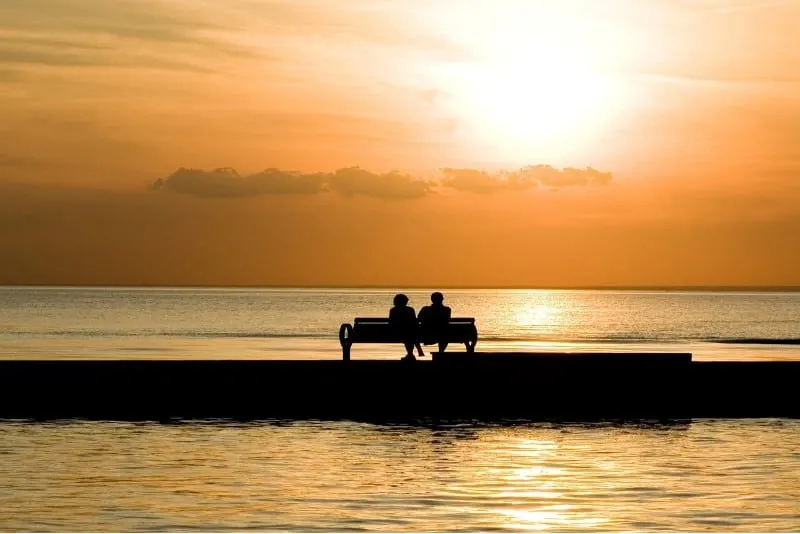 man and woman sitting on bench and watching sunset