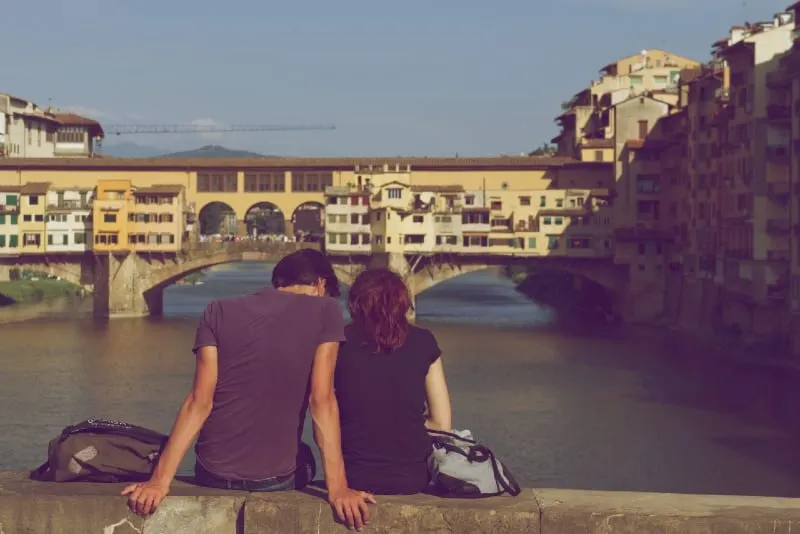 man and woman sitting on bridge looking at river