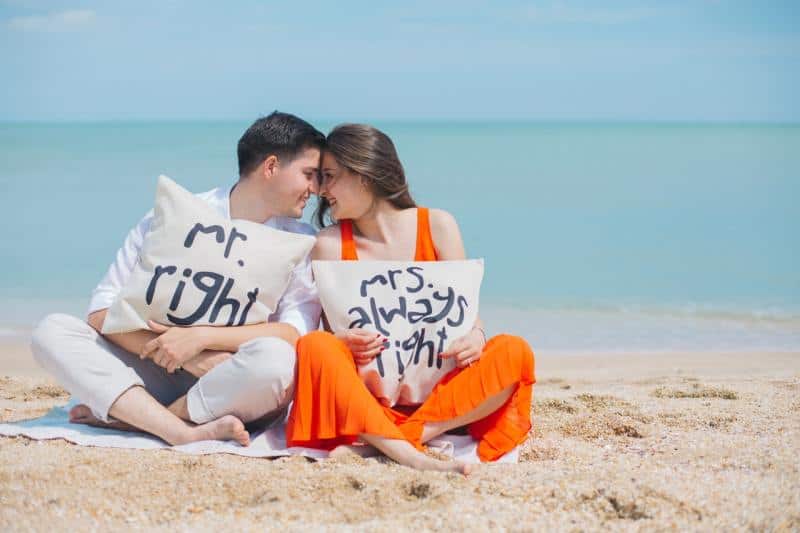 Coppia felice sulla spiaggia che tiene in mano pilows con messaggi divertenti