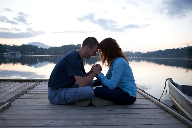 Couple praying while sitting on the dock by the lake