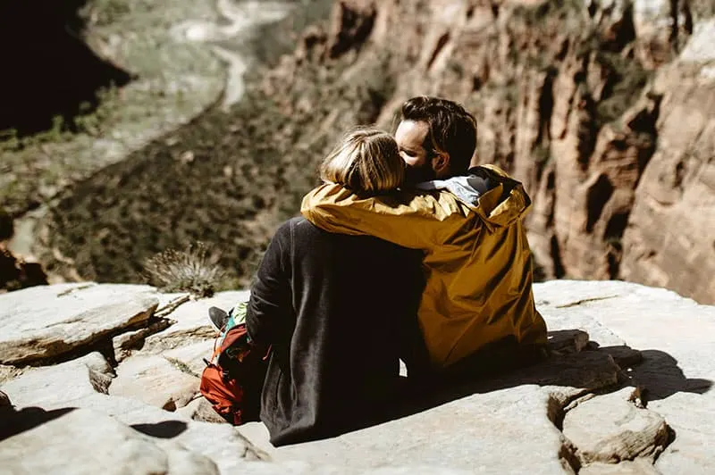 couple sitting on rocky ledge of mountain