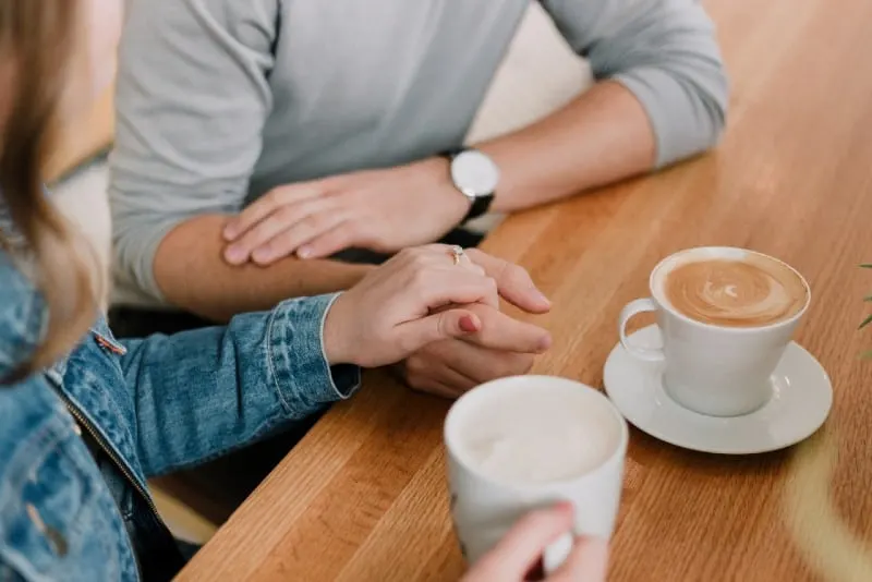 man and woman sitting at table while holding hands