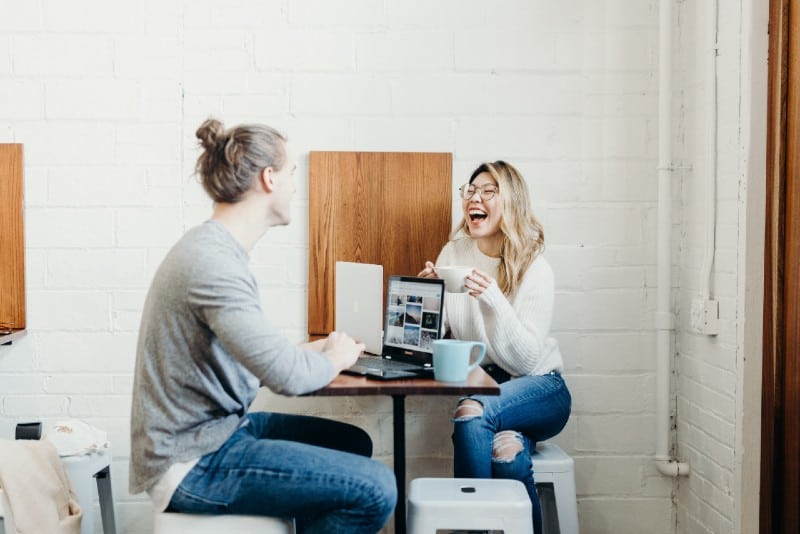 mujer sonriente y hombre con moño sentado a la mesa