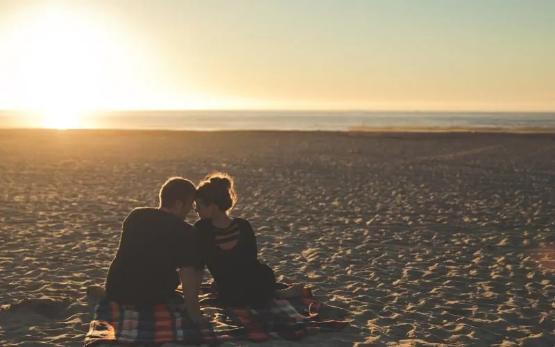couple sitting next to each other on the empty beach at sunset time
