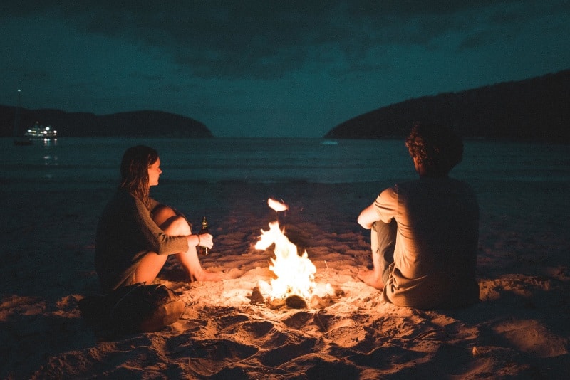 uomo e donna con fuoco di ossa seduti in riva al mare