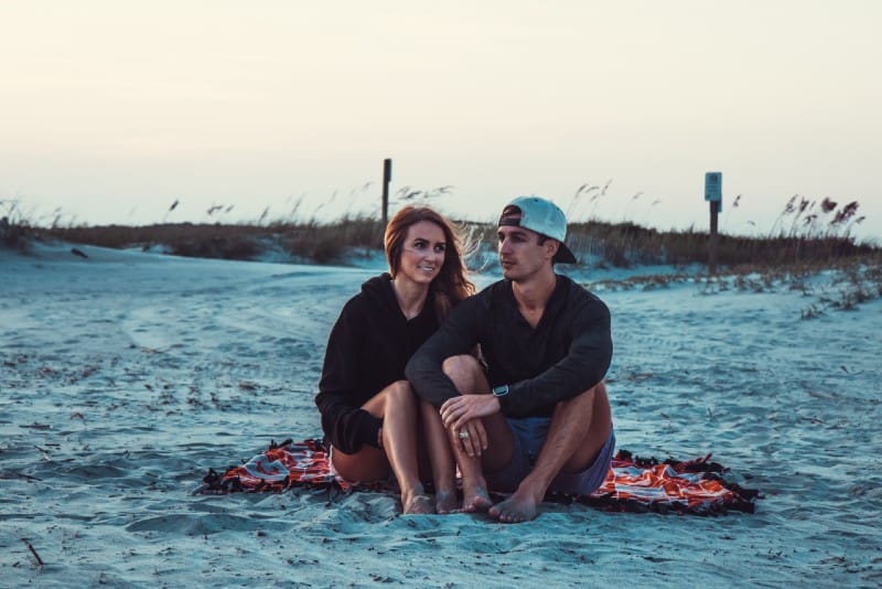 homem e mulher sentados numa manta na praia