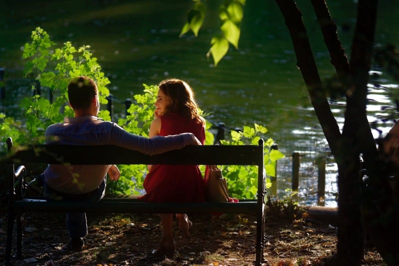 man and woman in red dress sitting on wooden bench