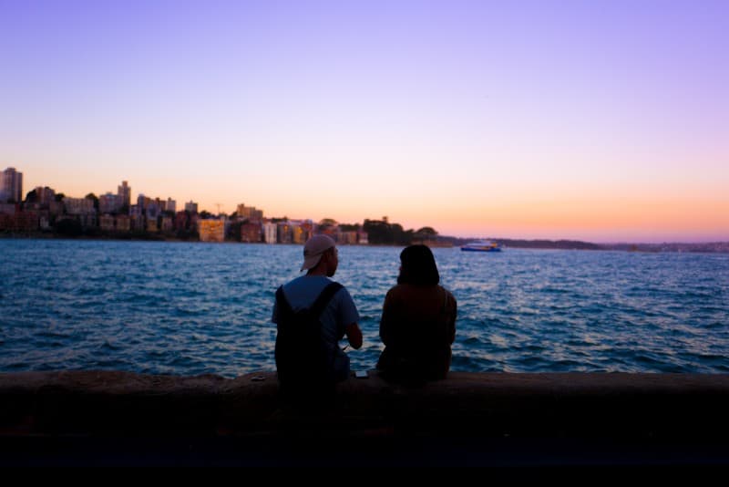 uomo e donna seduti su una banchina di cemento che guardano l'acqua
