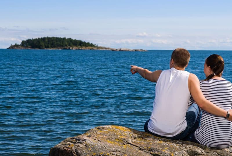 couple sitting on the rock gazing at an island in the middle of the sea