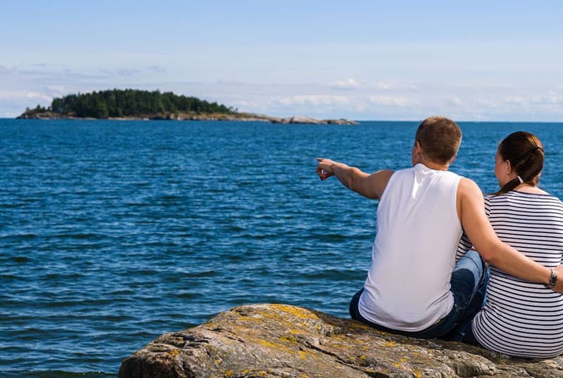 pareja sentada en la roca contemplando una isla en medio del mar