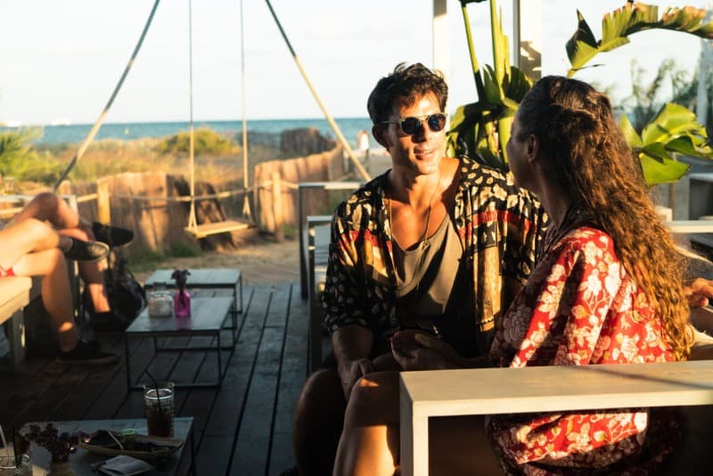 homem com óculos de sol e mulher sentados numa mesa ao ar livre