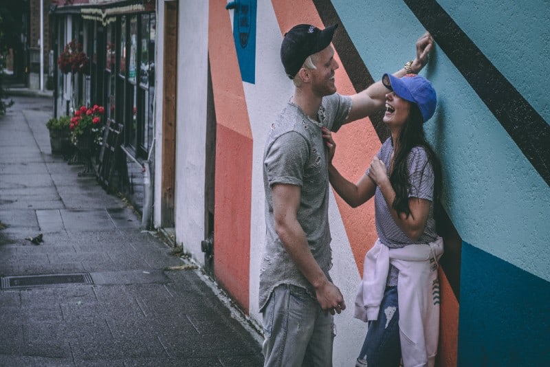 man and woman with caps leaning on wall