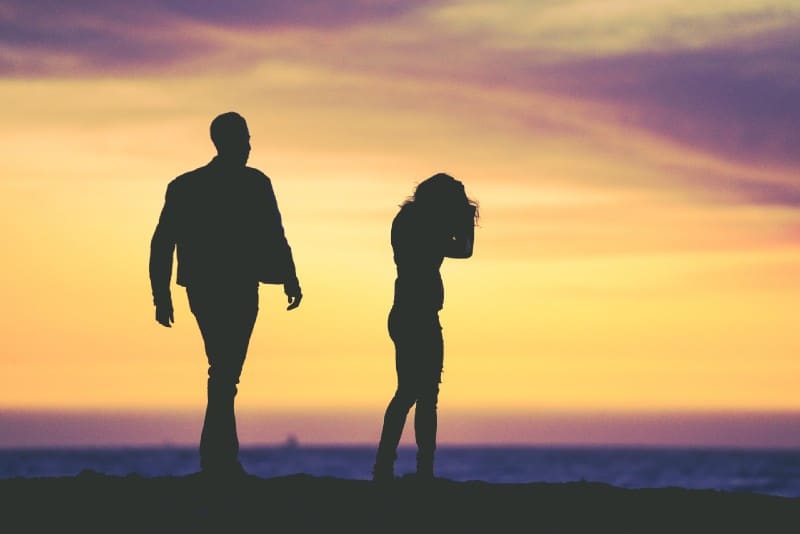 man and woman standing on beach during sunset