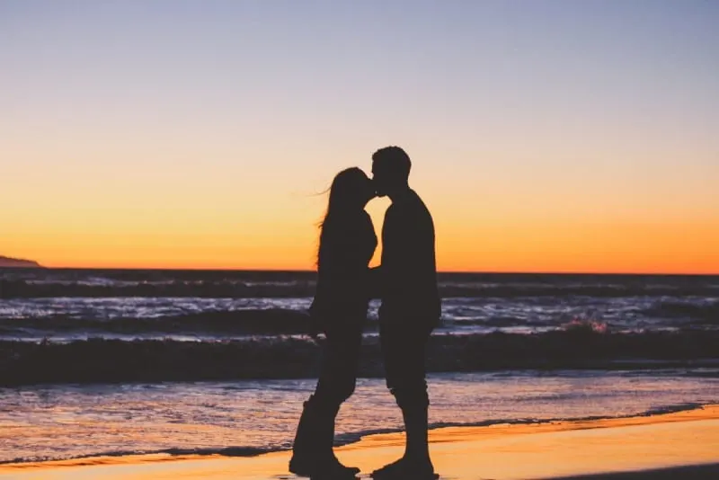 woman and man standing on beach and kissing