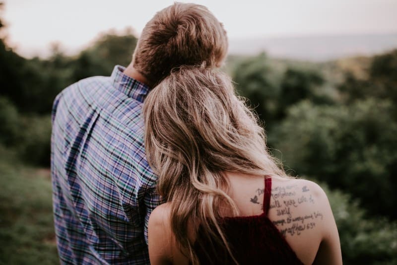 man and blonde woman with tattoo standing on mountain
