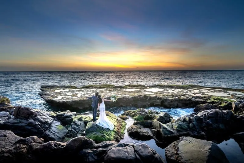 groom and bride standing on rock during golden hour