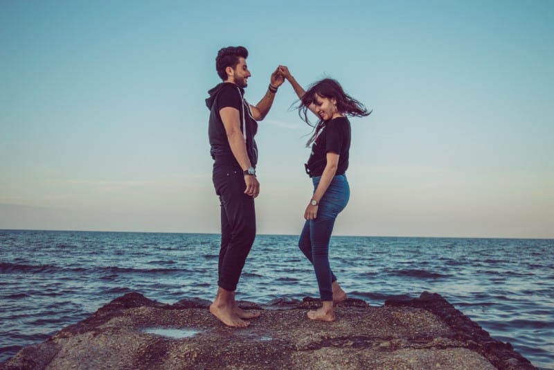 man and woman holding hands and standing on rock