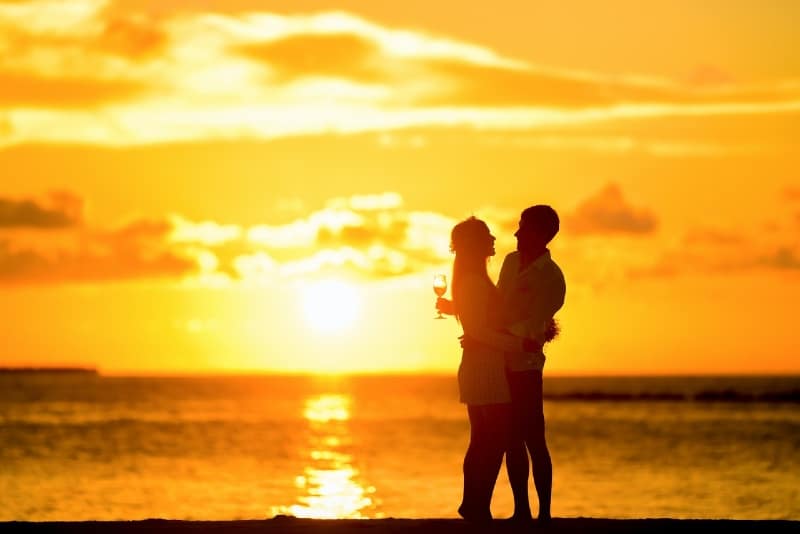 uomo e donna in piedi sulla riva del mare e abbracciati durante il tramonto