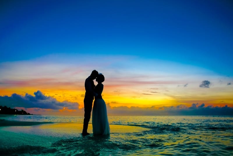 man and woman standing on seashore during sunset
