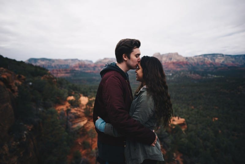 man in burgundy jacket kissing woman's forehead