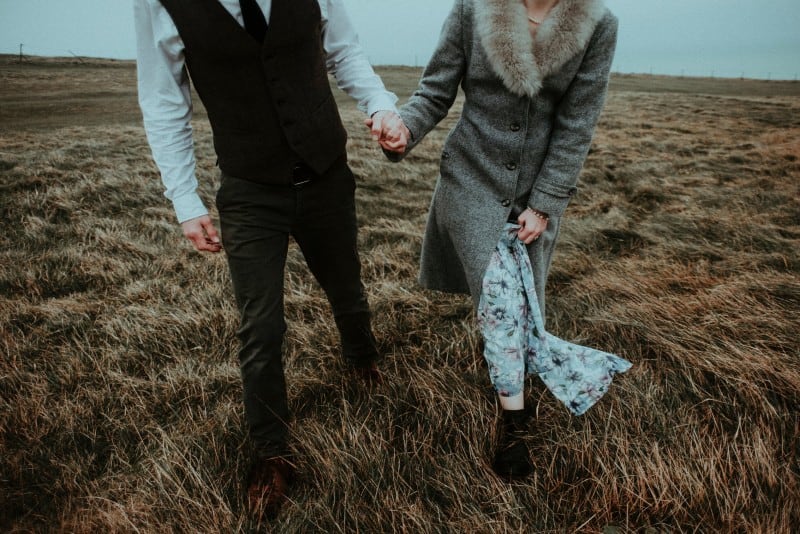 man and woman walking and holding hands in field